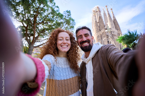 Photography Young caucasian couple taking a happy selfie in front of the sagrada familia, enjoying their vacation together, looking at camera smiling
