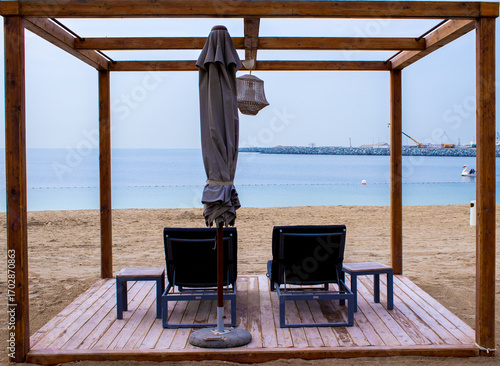 Relaxing beach chairs under wooden shade facing the sea, ideal for travel brochures, holiday ads, and leisure websites.
