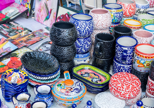A table full of colorful pottery and dishes. The table is covered with a variety of items, including bowls, cups, and vases. The scene is lively and vibrant. City of Puebla, Mexico, crafts