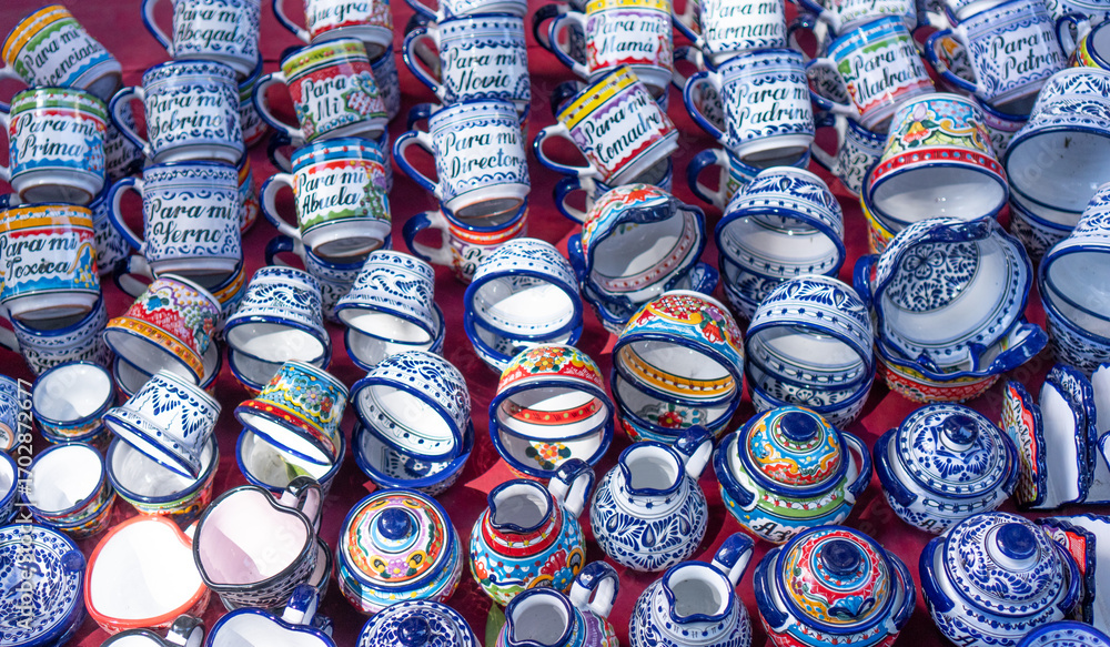 Fototapeta premium A collection of colorful cups and bowls with various designs and messages written on them. The cups and bowls are arranged in a row, with some of them being upside down. City of Puebla, Mexico, crafts