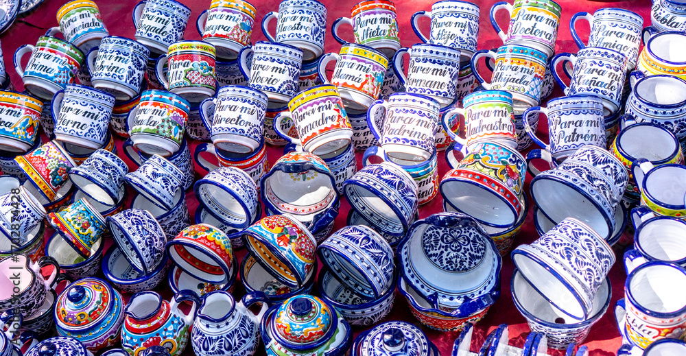 Fototapeta premium A large collection of colorful cups with Hebrew writing on them. The cups are arranged in a pile on a table. City of Puebla, Mexico, crafts