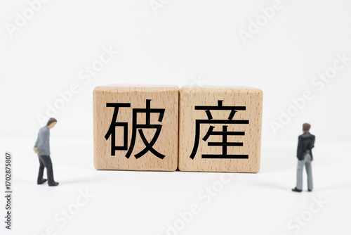 木製ブロックに破産の文字とミニチュアのビジネスマンのイメージ