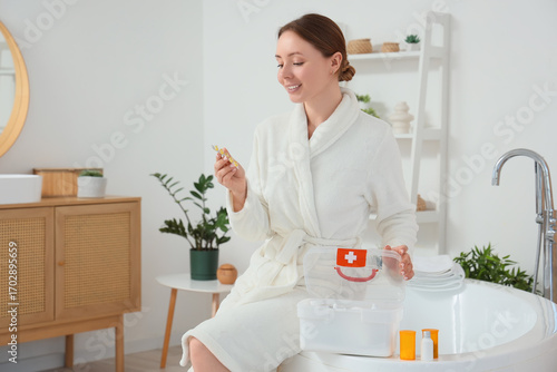 Young woman taking pills from first aid kit in bathroom