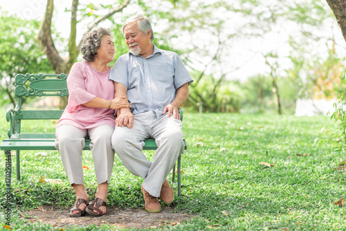 Happy smile mature senior Asain couple sitting on the bench in park enjoying retirement and spending time together. Elderly people love, care and relationship concept.