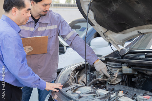 Mechanic taking photo of car damage while customer points at scratch, automotive inspection process for insurance claim or repair documentation, professional service detail in workshop scene
