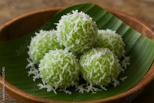 Indonesian klepon rice cake balls filled with palm sugar, coated in shredded coconut, served on banana leaf.