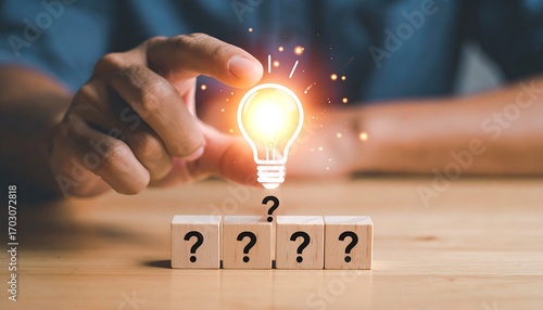 Hand holding lightbulb over question marks on wooden blocks