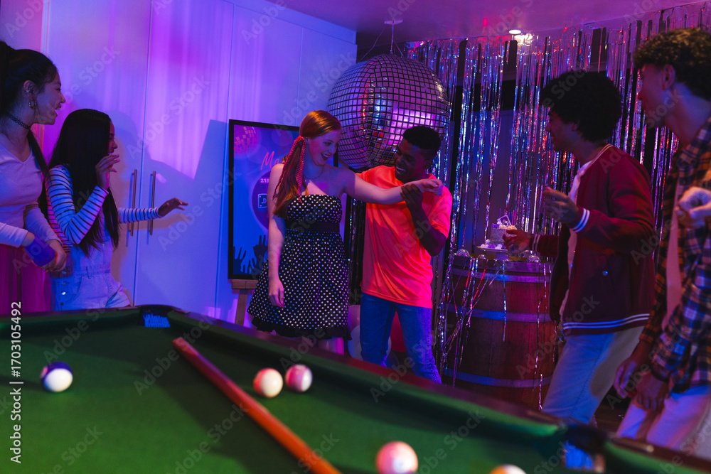 Fototapeta premium Teens celebrating at party, dancing near pool table under disco ball lights