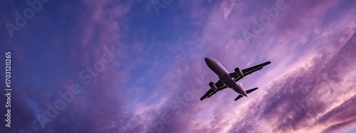 Modern passenger airplane flying high in colorful dramatic purple sky at sunset, concept of travel and transportation