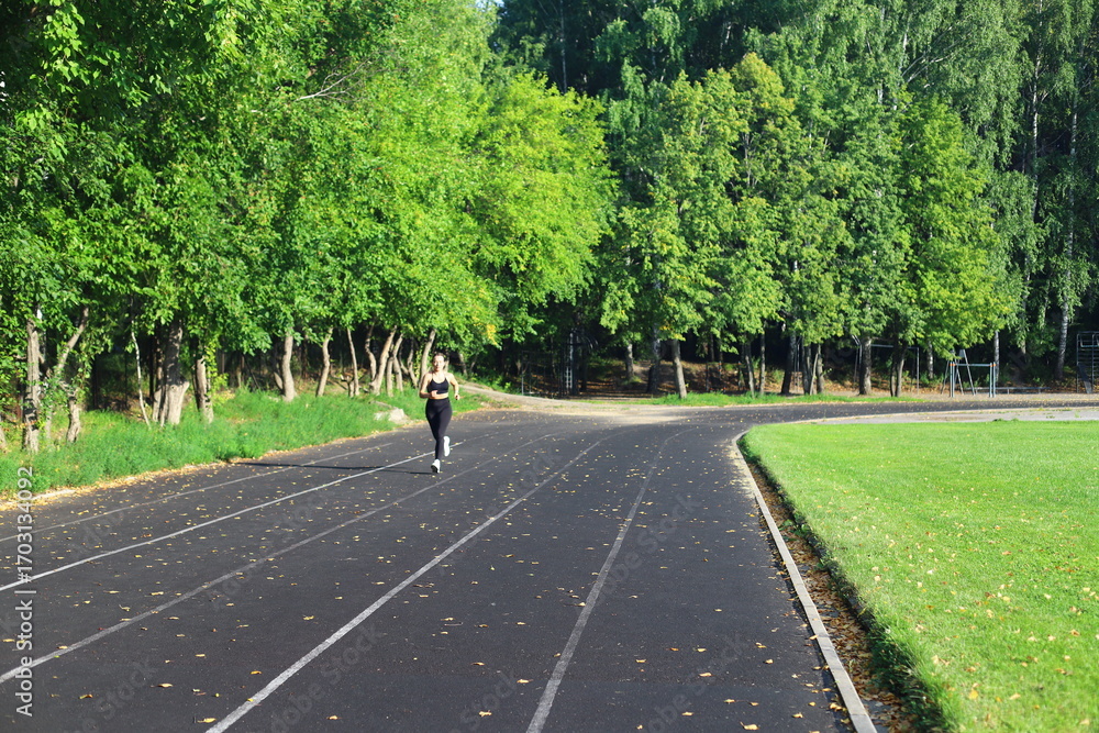 Fototapeta premium Athletic woman trains on outdoor stadium in summer day. Fitness workout.