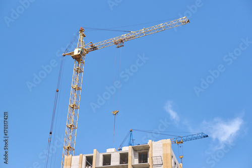 Tower cranes on construction site against clear blue sky with partial building view.