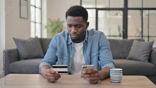 Financial Frustration: A man grapples with financial concerns, staring intently at a credit card and a smartphone in a realistic depiction of modern-day challenges.