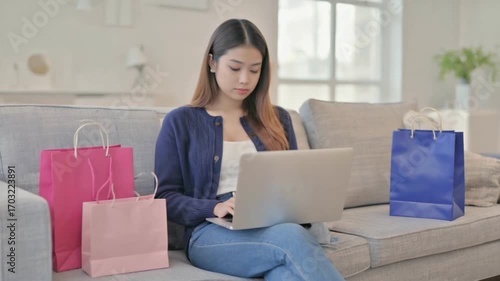 Digital Shopping at Home: An Asian woman sits comfortably on her sofa at home, shopping online with her laptop. The setting showcases a lifestyle of comfort and convenience.
