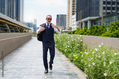 Elderly businessman walking in city with coffee cup. Urban lifestyle and professional senior.