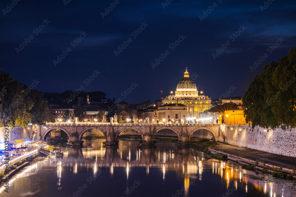 Fototapeta premium Illuminated St. Peter's Basilica in Vatican City with the glowing Ponte Sant'Angelo bridge reflecting in the Tiber River at night, symbolizing faith, history, and timeless Roman beauty