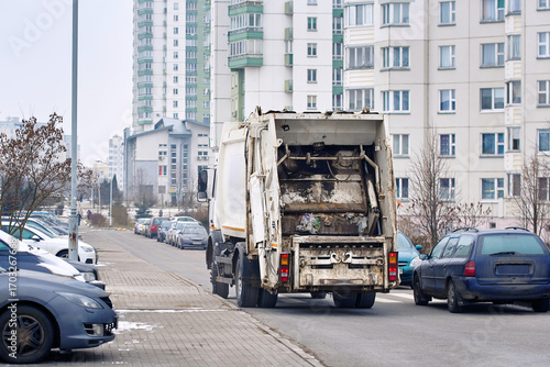 Obraz na plátně Garbage truck driving through residential district during winter season, municipal waste collection service on urban street with homes and frozen environment in background