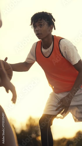 Junior streetballers training in park, vertical portrait of black sportsperson exercising with ball, basketball players practicing together in outdoors court in summer vacation, brothers or friends