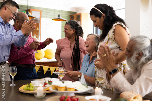 Celebrating at home, senior friends sharing laughter and drinks around table
