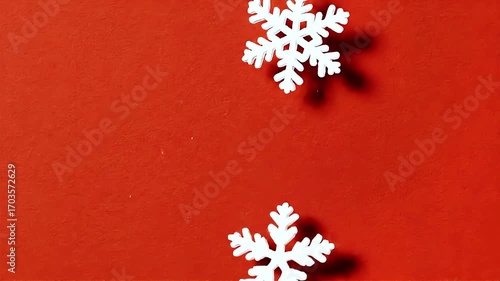 White snowflake cutouts falling onto red background in slow motion
