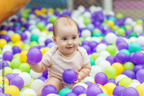 Smiling baby playing in colorful ball pit. Early development