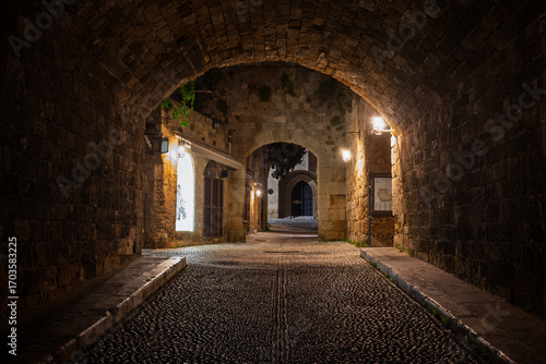 Fototapeta Naklejka Na Ścianę i Meble -  Idyllic and empty cobblestone street and tunnel at the medieval UNESCO World Heritage Site of Old Town of Rhodes on Rhodes island in Greece at night.
