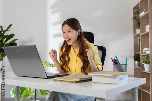 Asian Young woman celebrating success while working on laptop at home office, happy female student excited with online learning achievement