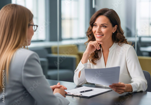 Career Interview and Appraisal: Capturing a moment of professional evaluation. Two businesswomen engage in a career interview within a modern office environment.