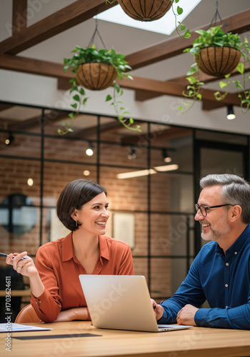 Collaborative Office Discussion: Two professionals engage in a focused discussion around a laptop in a modern office setting.