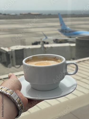Cup of coffee at the airport before flight. Travel moment with airplane in background and warm drink in focus.