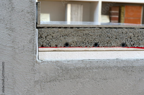 A cutaway view shows the layers of a building's structure, including concrete, insulation, and radiant heating pipes, during the construction or renovation process.