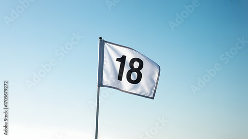 Golf flag marking eighteenth hole waving in wind against blue sky on sunny day outdoors golf