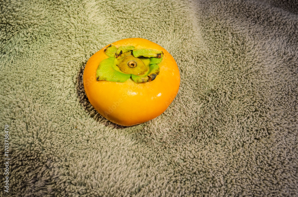 Naklejka premium Ripe persimmon fruit isolated, top view, fluffy gray fabric background.