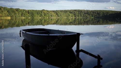Time lapse of a drifting moored rowboat at Caputher See in Brandenburg, Germany, reflecting calm water and forest at dusk.