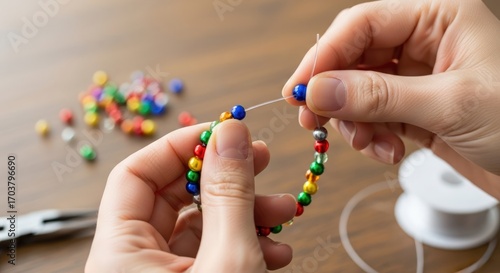Close-up of hands stringing colorful beads onto a thread to create a bracelet.