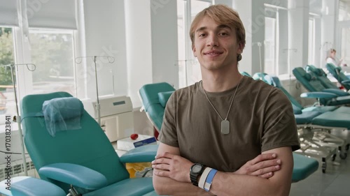 Portrait of young smiling male soldier in military uniform posing for camera after donating blood in clinic