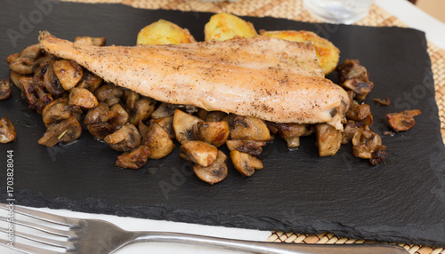 fried trout fillet on pillow of fried champignon mushrooms on dark warm stone plate