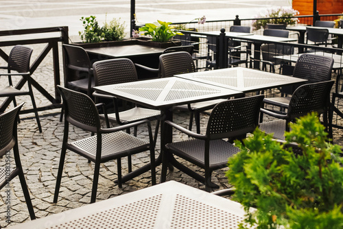 Outdoor cafe with empty black chairs and tables. Modern restaurant terrace with metal furniture. Urban dining area waiting for guests.