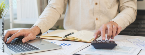 Account finance, asian young business man hand using calculator, laptop computer for calculate budget, cost and income of company from paperwork, plan spend money expenses, working on desk at home.