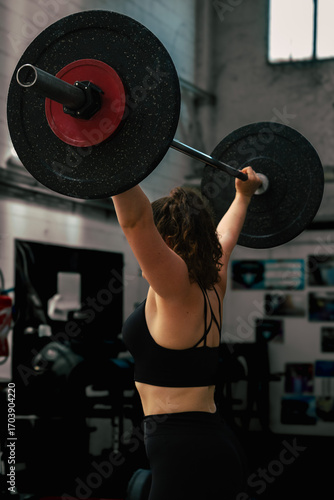 Fototapeta Femme soulevant une barre olympique en salle de sport