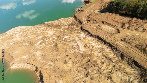 Aerial view of a brown earth excavation site near a calm water body, showcasing ongoing construction and land development practices, reflecting environmental impact.
