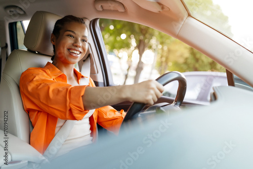 Fotografie Happy African American woman driving car with wide smile, showing joy and confidence