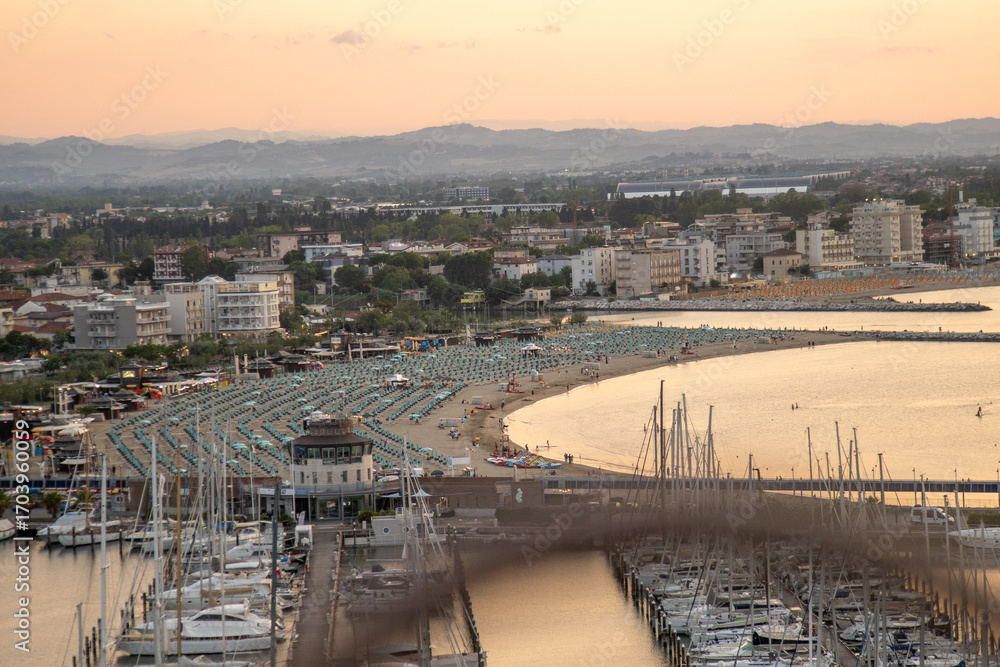 Fototapeta premium Seaport of Italian city of Rimini. Wide sandy sea beach resort with sun loungers and umbrellas on coast top view. Hotels apartments. Port Italy