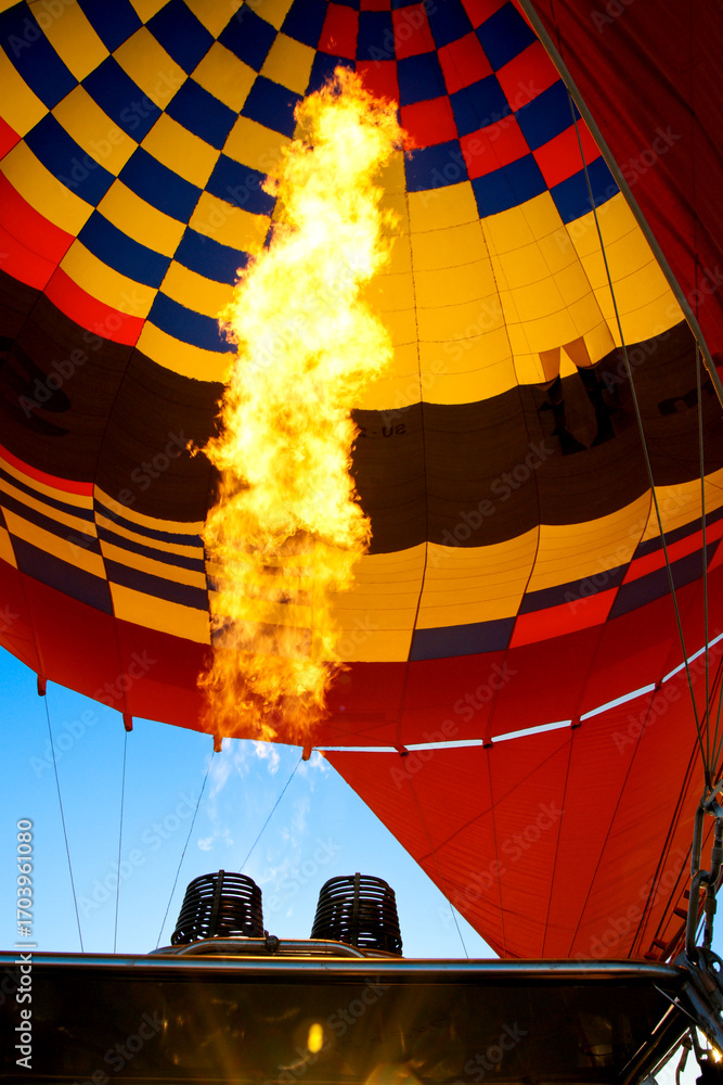 Obraz premium A vibrant hot air balloon with flames rising from the burner, creating a stunning contrast against the colorful canopy.