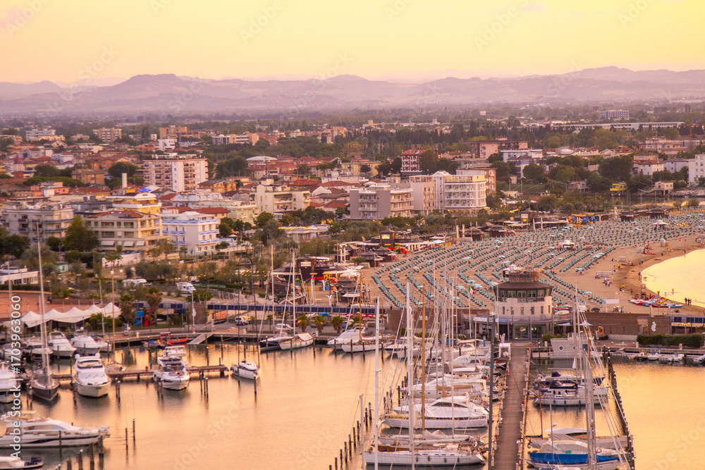 Obraz premium Sea port of Italian city of Rimini beach resort on coast top view. Hotels apartments. Italy holidays. Yachts and ships in the bay at sunset in the evening