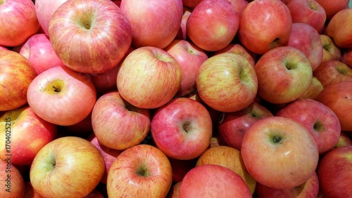 This is a close-up shot of a large pile of apples. The apples are a mix of red and pink with hints of yellow and green, suggesting a variety like Gala or Fuji.