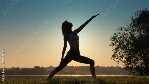 A woman gracefully practices yoga during a vibrant and breathtaking sunrise, which symbolizes tranquility, mindfulness, and a profound connection with the beauty of nature all around her