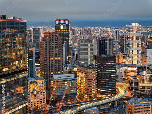 Illuminated cityscape of Osaka at dusk, featuring skyscrapers, highways, and urban lights, Japan.