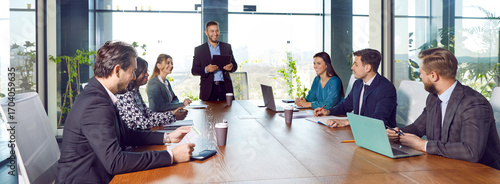 Fotografie Diverse joyful confident people sitting at big table in meeting room having business conference in modern office
