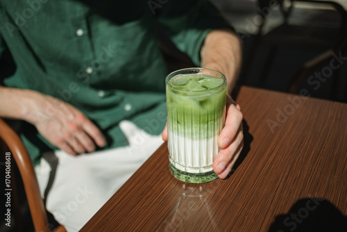 Close-up of a mid adult man sitting at an outdoor cafe drinking an iced matcha latte on a summer day