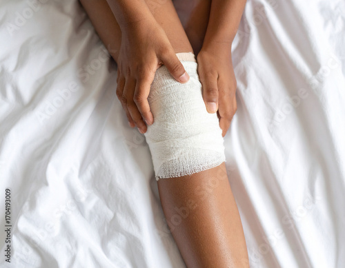 Injured Knee with Bandage on White Bedding, Close-Up View